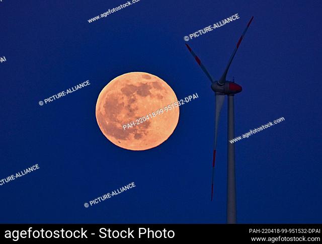 16 April 2022, Brandenburg, Petersdorf: The full moon shines at dusk next to a wind turbine in East Brandenburg. Photo: Patrick Pleul/dpa