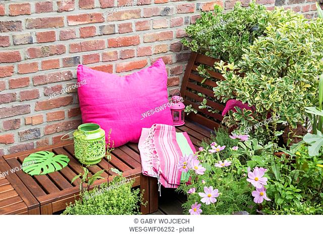 Balcony with bench, pink cushion, blanket, lanterns and various potted plants