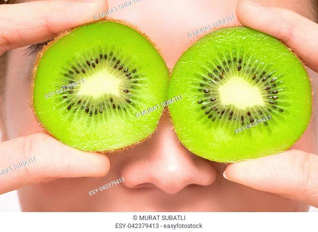 Woman with kiwi slices in front of her eyes