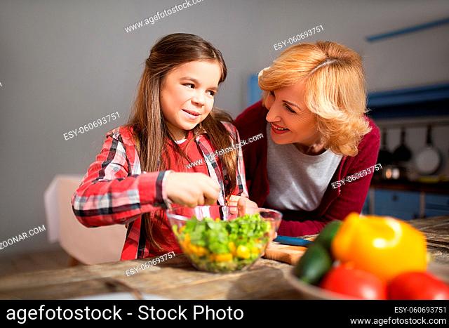 Little girl is happy after preparing salad by herself. Her granny is proud of her