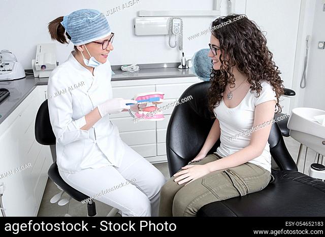 Friendly woman in medical uniform smiling and demonstrating teeth brushing technique to cheerful female patient during work in modern clinic