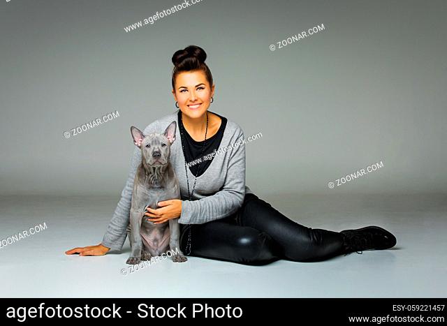 beautiful young woman holding thai ridgeback puppy dog on arms. studio shot on grey background. copy space