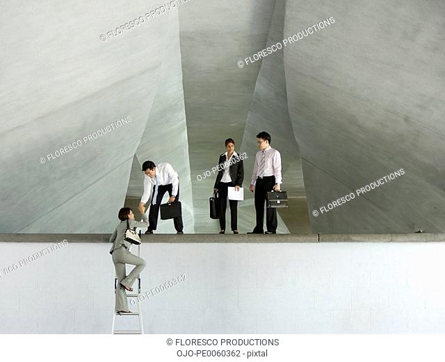 Businessman in structure helping businesswoman up ladder with two businesspeople watching