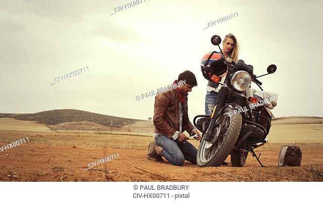 Young couple repairing motorcycle in remote countryside field