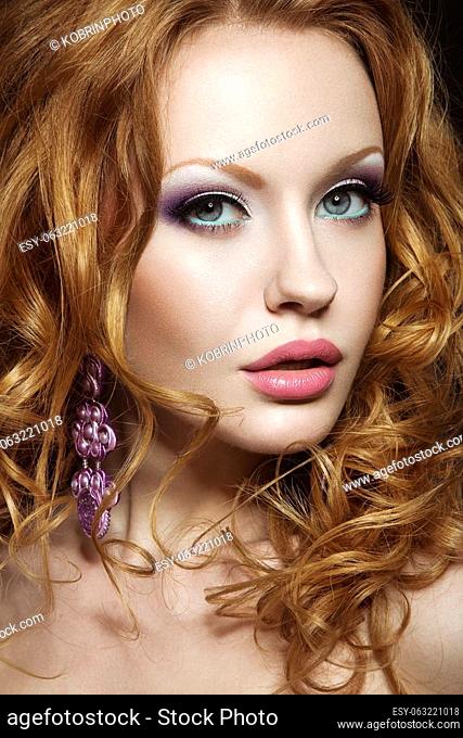 Beautiful red-haired girl with bright makeup and curls. Picture taken in the studio on a black background