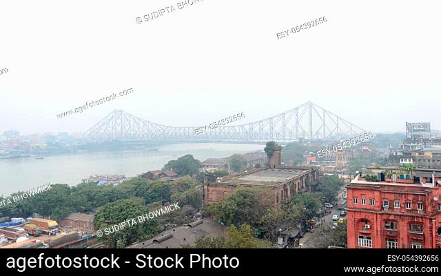Aerial view Cityscape Howrah Bridge (Rabindra Setu) of Calcutta city life on Hooghly riverside near Burrabazar area on a foggy winter evening day