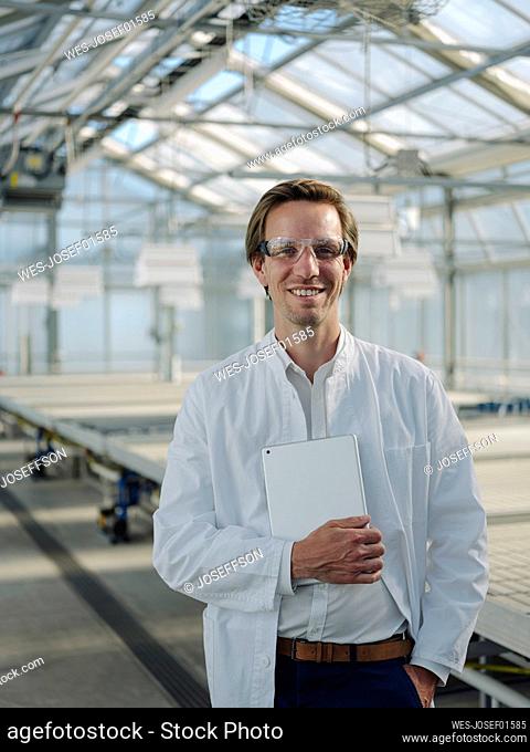 Portrait of a smiling scientist holding tablet in a greenhouse