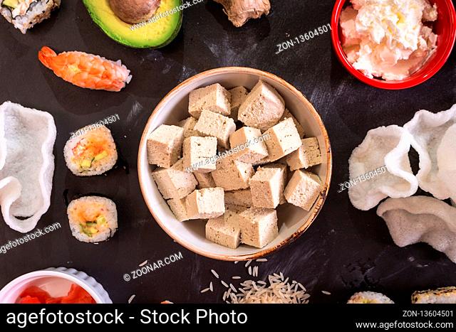 Overhead shot of tofu cheese and sushi on a dark background