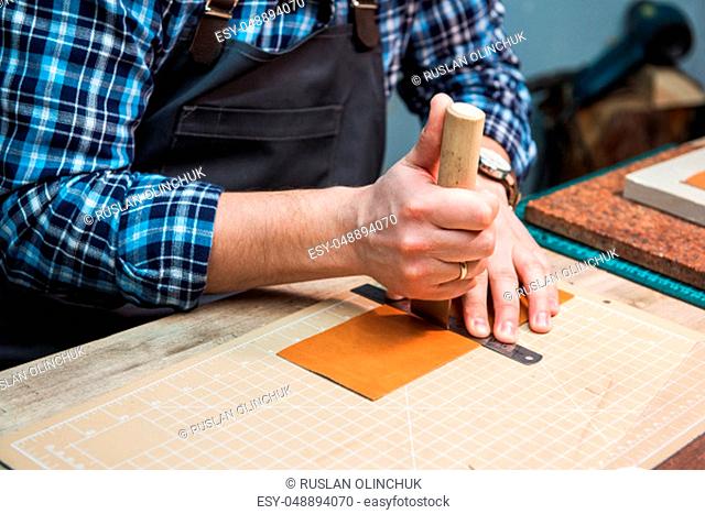 Man working with leather textile at a workshop. Craftman cutting leather. Concept of handmade craft production of leather goods