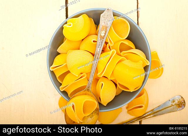 Raw Italian snail lumaconi pasta on a blue bowl over rustic table macro