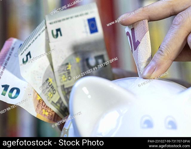 ILLUSTRATION - 23 October 2023, Saxony, Leipzig: ILLUSTRATION - A woman puts a 10 euro bill into a piggy bank. October 30
