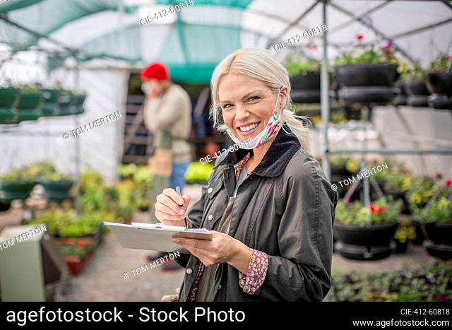 Portrait happy female garden shop owner with clipboard in greenhouse