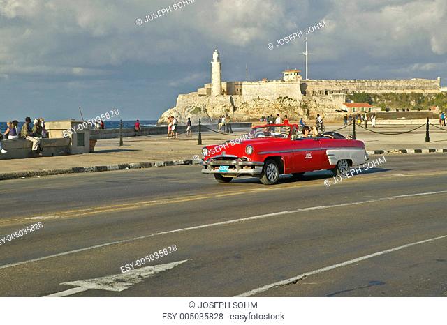 American red convertible car driving past the Castillo del Morro across the Havana Channel, Cuba