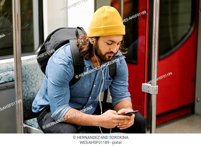 Man with backpack listening music with smartphone and earphones in commuter line, Berlin, Germany