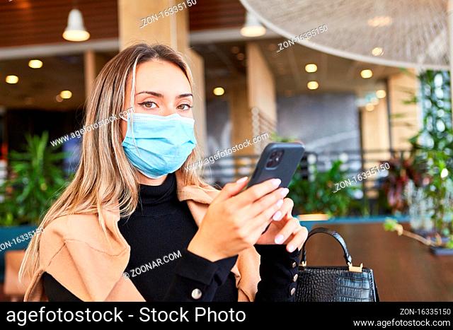 Frau mit Mundschutz wegen Covid-19 sitzt mit Smartphone in einem Restaurant
