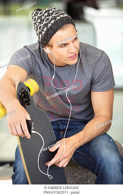 Man holding a skateboard and listening to music on a mobile phone