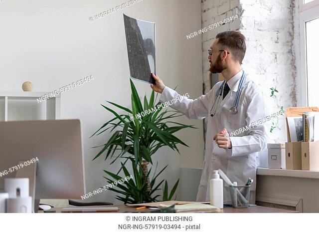 Closeup portrait of intellectual man healthcare personnel with white labcoat, looking at brain x-ray radiographic image, ct scan, mri, clinic office background