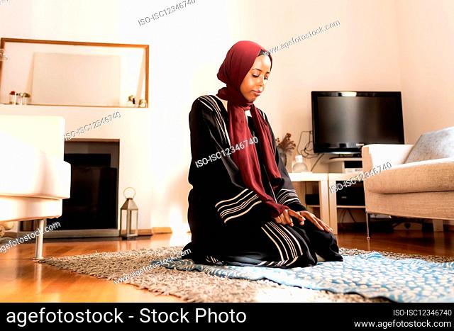 Young muslim woman, kneeling during prayer