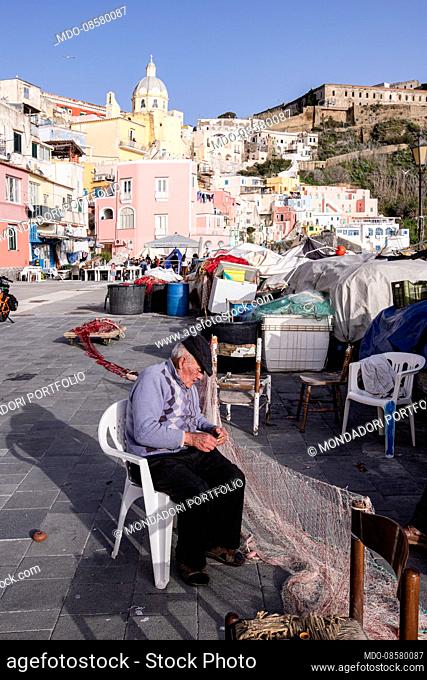 An old fisherman fixes his nets in the Corricella marina. Procida (Italy), February 6th 2021