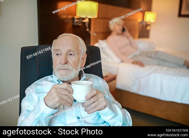 Morning coffee. Senior bearded man having his morning coffee and looking thoughtful
