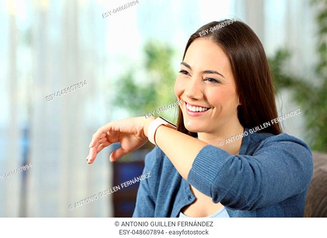 Happy woman talking to a smartwatch sitting on a couch in the living room at home