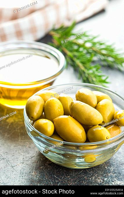 Green olives and olive oil in glass bowl on old kitchen table