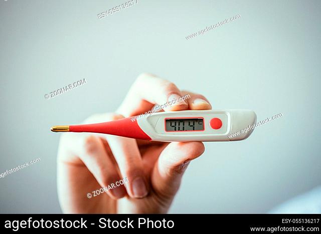 Man is holding a fever thermometer in his hand