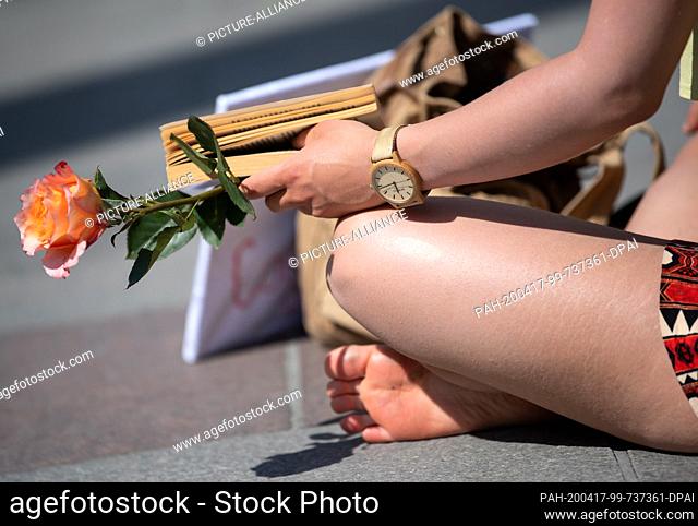 17 April 2020, Bavaria, Munich: A participant of the rally ""Reading for Democracy"" sits barefoot on Marienplatz, holding a rose in her hands