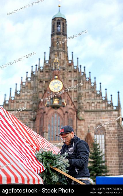 21 November 2023, Bavaria, Nuremberg: An employee of the wooden toy maker Graupner from the Erzgebirge attaches a garland of brushwood to the stand during the...