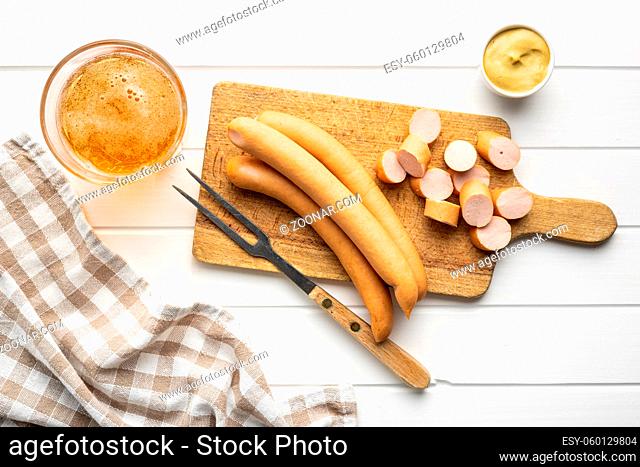 Sliced smoked frankfurter sausages on cutting board on white table. Top view