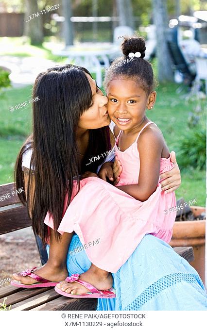 A mixed race mother kisses her smiling daughter on the cheek
