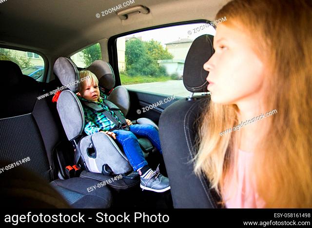 Mom need to drive a car and looks back at her baby. The mom touches her crying baby