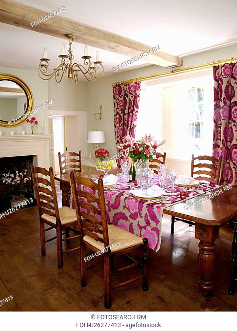 Ladderback chairs at table set for lunch in country dining room with pink cut-velvet Designer's Guild curtains and cloth