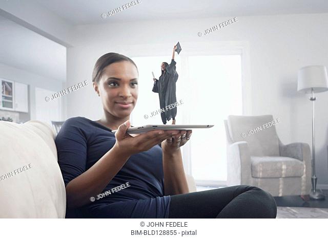 Black woman watching figure of graduate standing on digital tablet