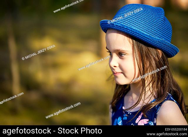 adorable little girl in a blue hat posing in the spring pine forest