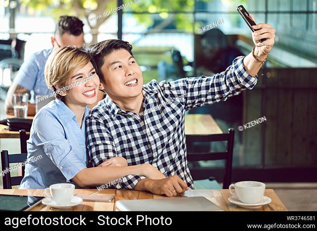 Portrait of young couple taking selfie in the cafe through cellphone
