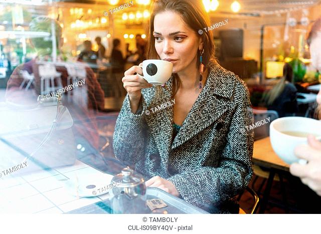 Young woman drinking coffee with friend in cafe, London, UK