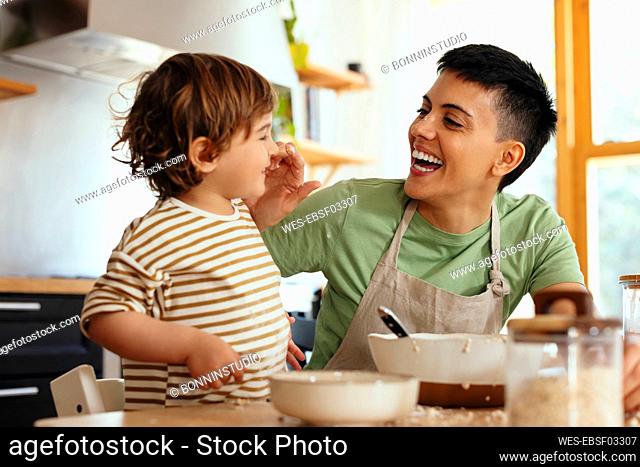 Happy woman touching son's nose in kitchen at home