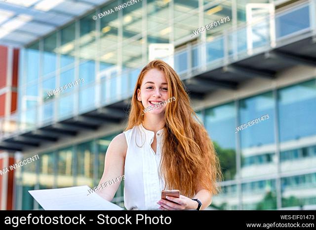 Beautiful female freelancer with document in front of building