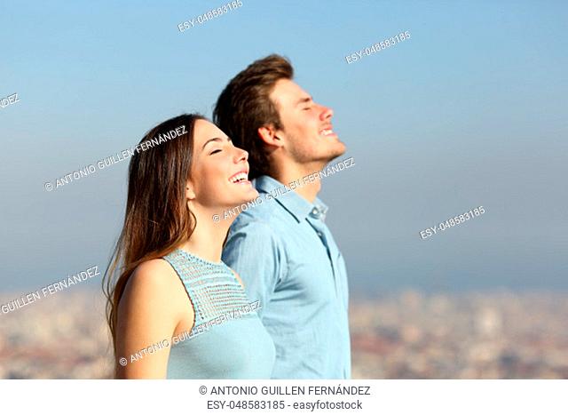 Side view portrait of a happy couple breathing fresh air with an urban background