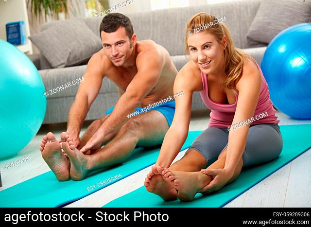 Young couple sitting on fitness mattress and streching legs before treining