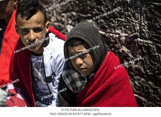 29 June 2018, Spain, Tarifa: Young migrants from North Africa sit at the port of Tarifa covered in red blankets after being rescued from the Strait of Gibraltar
