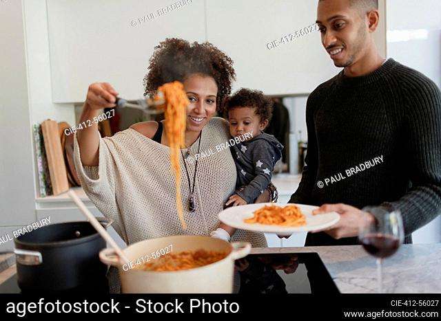 Parents with baby daughter cooking spaghetti at kitchen stove