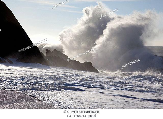 Sunlight shining on large waves crashing against rocks