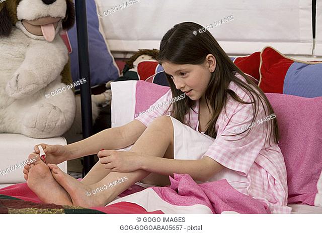 Young girl painting her toenails in bed