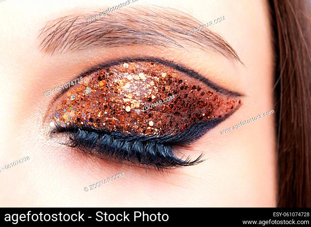 Close-up shot of female face with vogue golden shining eyes makeup. Eye closed