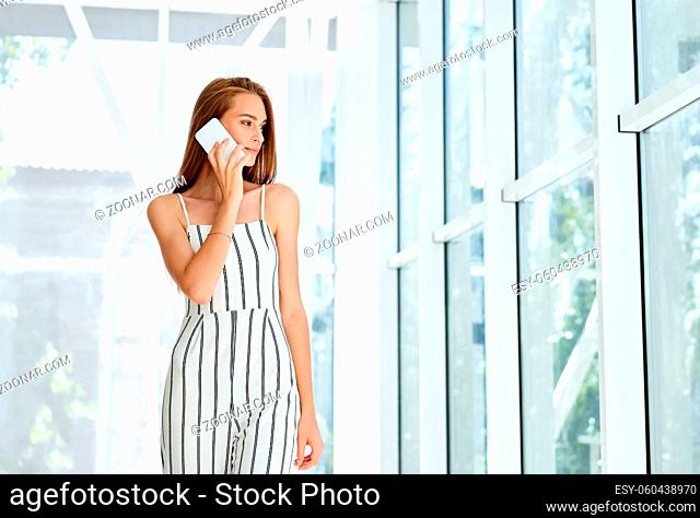 Smiling pretty businesswoman talking on phone in open space modern office with panoramic windows background. Copy space. Communication