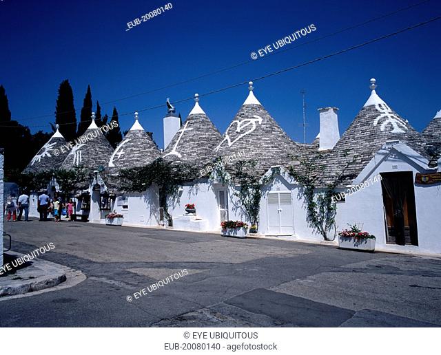 White Trulli buildings with runic symbols painted on the grey stone roofs in Alberobello village that have been converted into houses and a shop