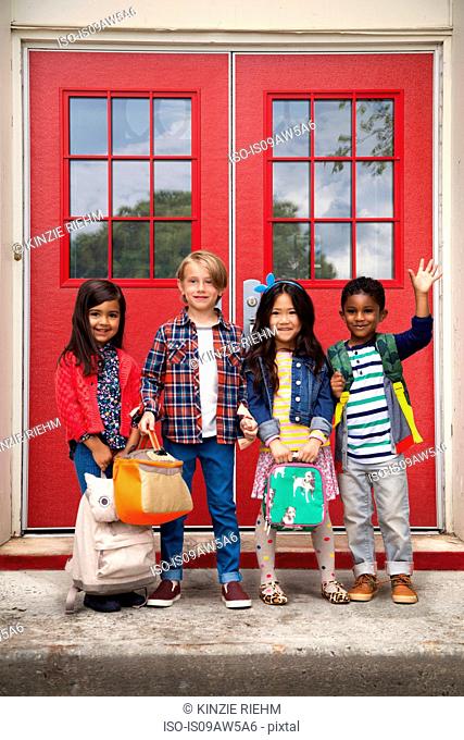 Portrait of elementary schoolgirls and boys waving from elementary school doorway