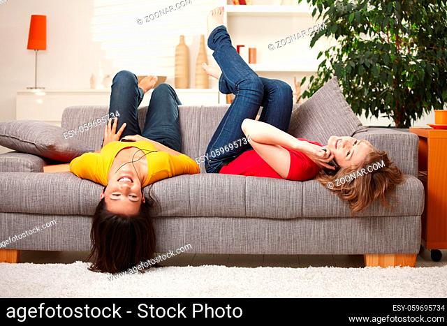 Happy teen girls resting on sofa at home, smiling